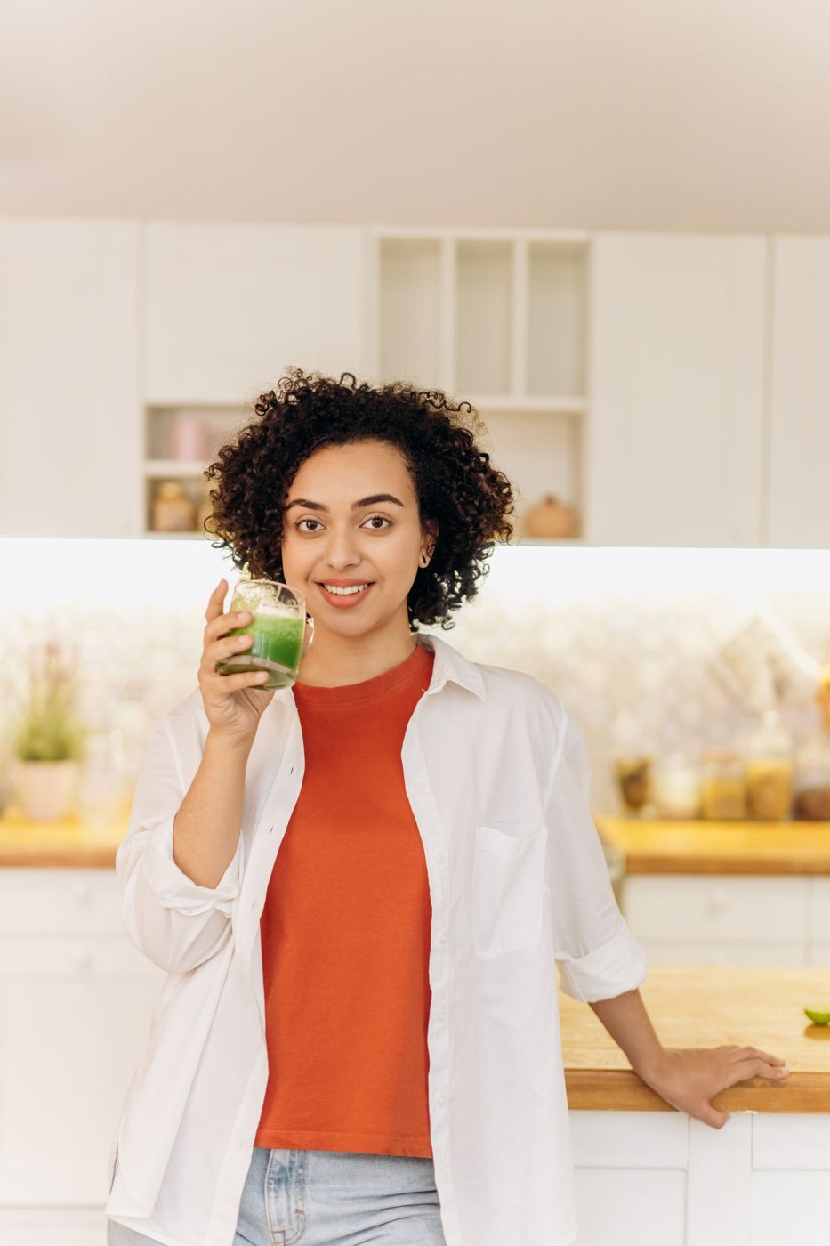 Mulher sorridente com um copo de batido verde na cozinha